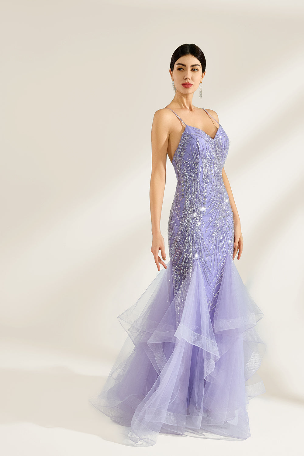 A woman stands against a light background, wearing a lavender mermaid gown. It has thin straps, a deep V - neckline, and is adorned with intricate silver bead patterns. The layered tulle skirt adds a romantic touch, perfect for formal events like galas or weddings, exuding elegance and charm.5