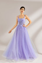 The model has her hair neatly styled and wears long, elegant earrings. The dress is lavender. It features a square neckline with spaghetti straps, and the bodice is adorned with delicate lace. The skirt is made of flowing tulle, creating a dreamy and elegant look, perfect for formal occasions.3