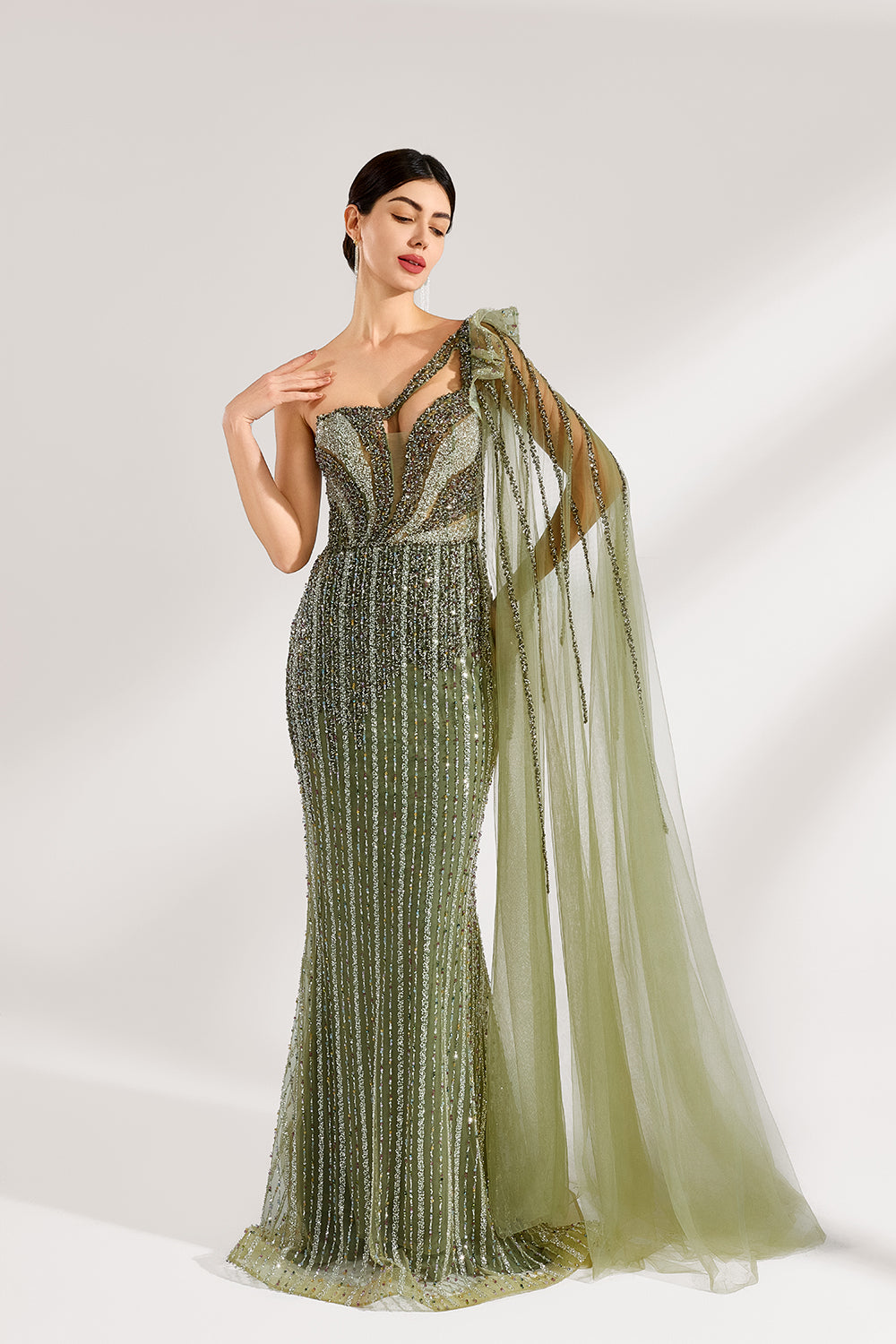 Illuminated softly, a woman captivates in an olive - green one - shoulder evening gown. The sequined mermaid silhouette, paired with a tulle cape, creates a striking and elegant look for formal events.3