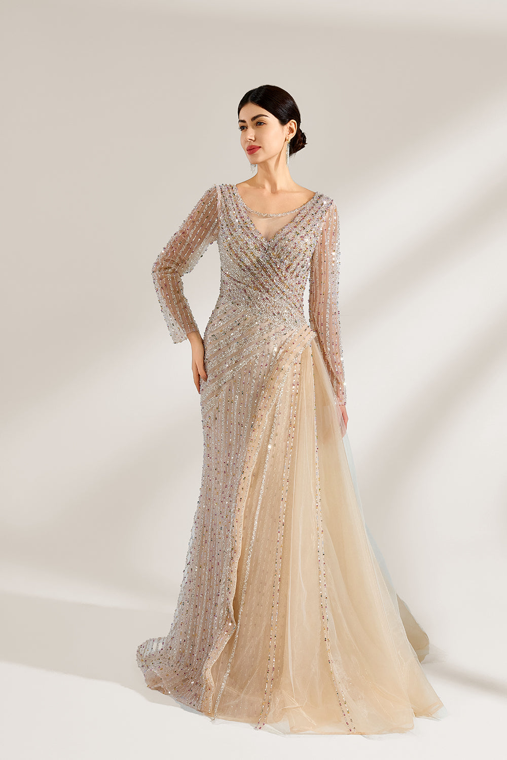 Bathed in soft light, a woman exudes elegance in a light beige sequined evening gown. With long sleeves, a criss - cross V - neck, and tulle - paneled skirt, it creates a glamorous and refined look for formal events.1