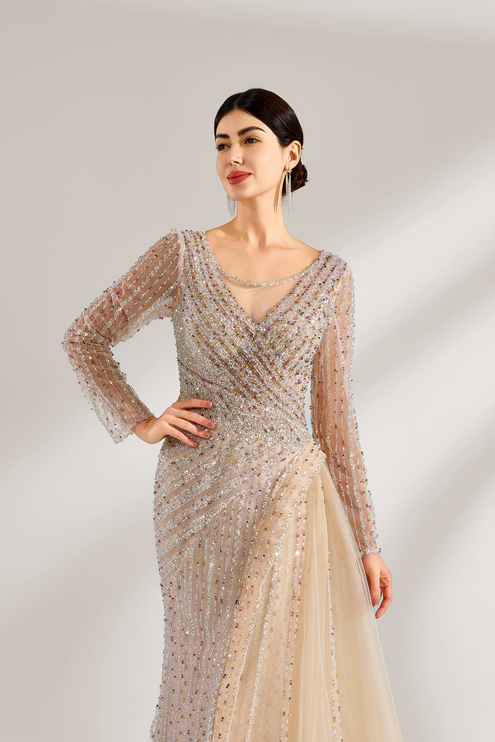 Bathed in soft light, a woman exudes elegance in a light beige sequined evening gown. With long sleeves, a criss - cross V - neck, and tulle - paneled skirt, it creates a glamorous and refined look for formal events.4