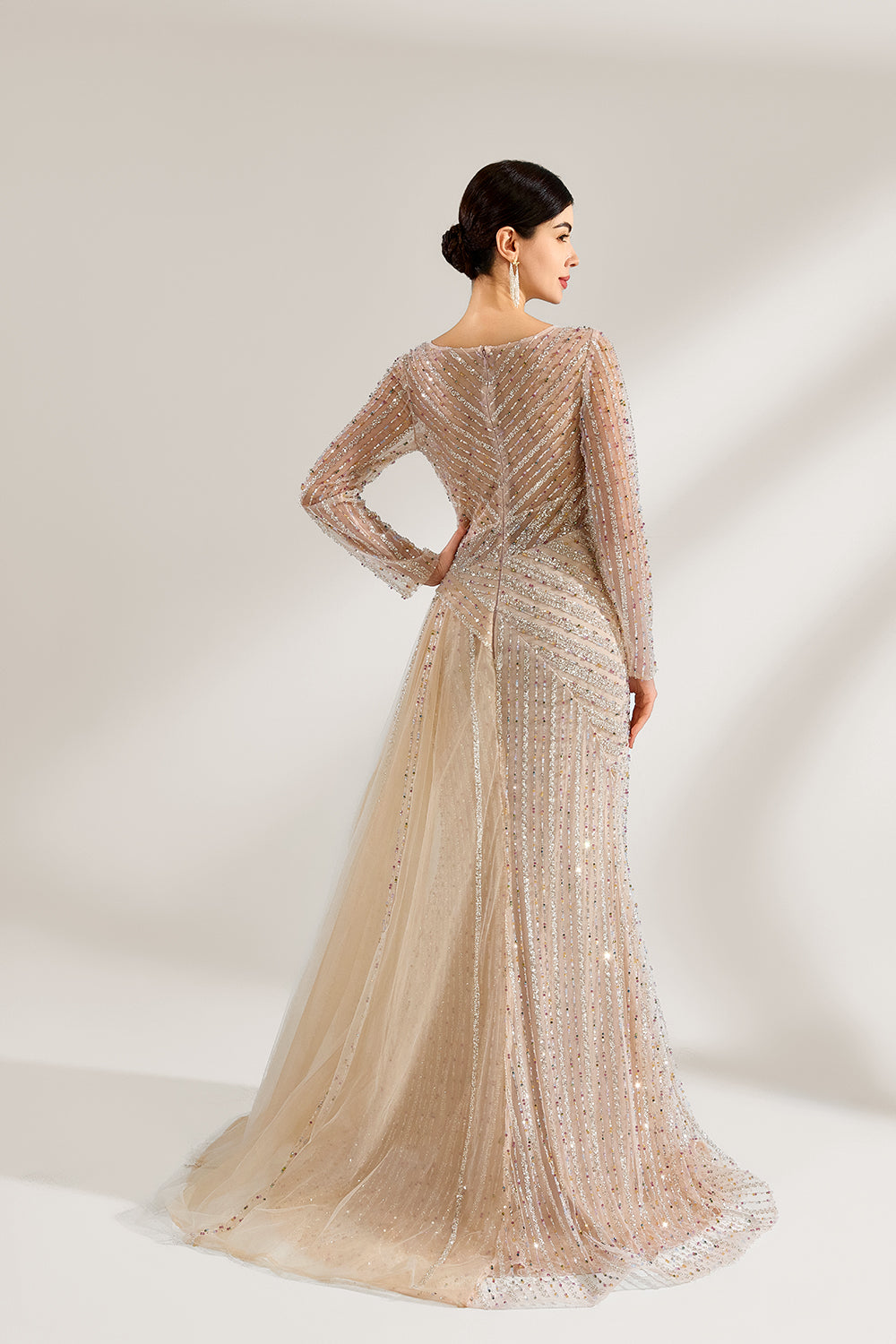Bathed in soft light, a woman exudes elegance in a light beige sequined evening gown. With long sleeves, a criss - cross V - neck, and tulle - paneled skirt, it creates a glamorous and refined look for formal events.2