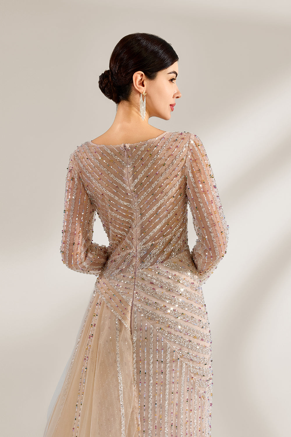 Bathed in soft light, a woman exudes elegance in a light beige sequined evening gown. With long sleeves, a criss - cross V - neck, and tulle - paneled skirt, it creates a glamorous and refined look for formal events.5