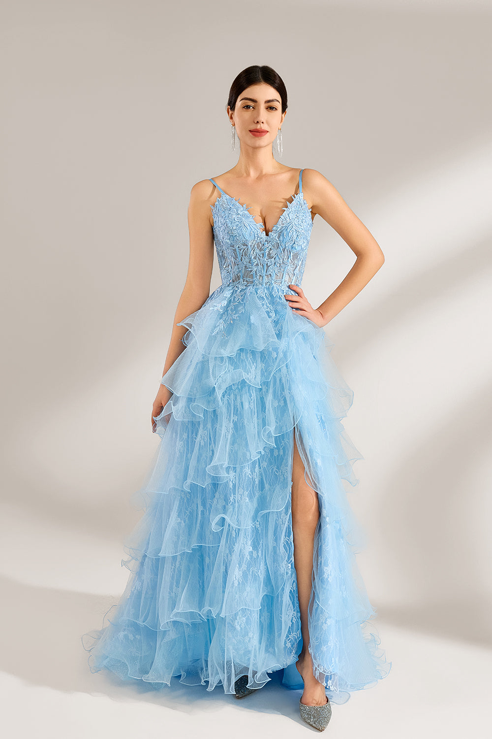 A woman stands against a light background, wearing a light - blue tulle gown. It has thin straps, a deep V - neckline, and intricate lace embroidery on the bodice. The layered, ruffled skirt with a high side slit creates a romantic and glamorous look, perfect for formal events like proms or weddings, exuding elegance and charm.1