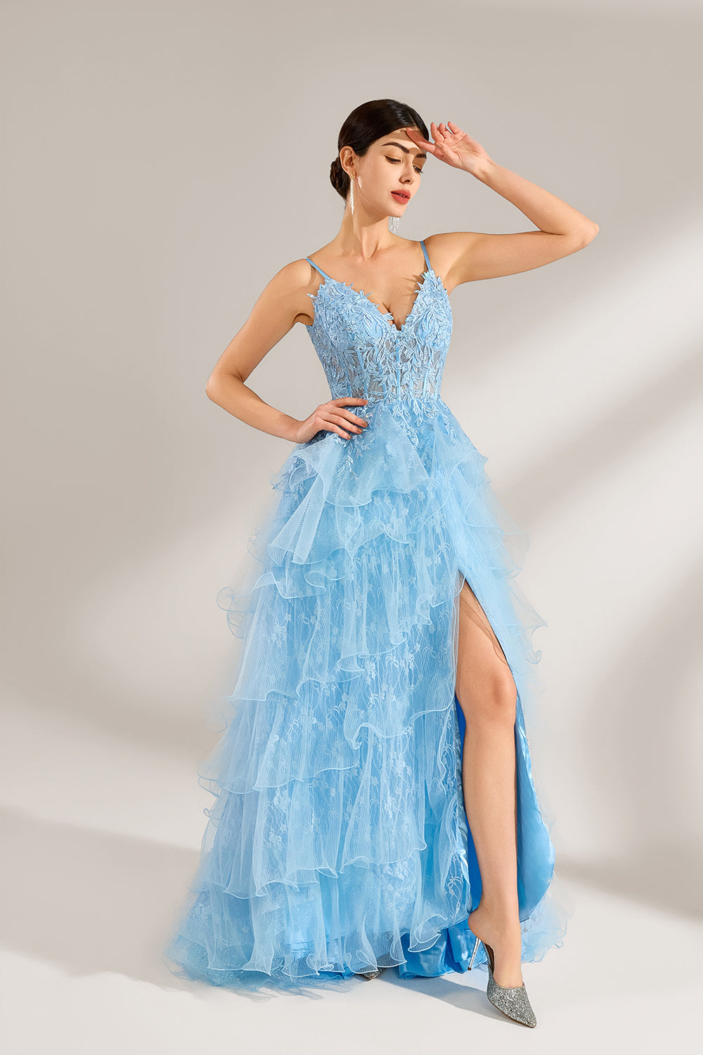 A woman stands against a light background, wearing a light - blue tulle gown. It has thin straps, a deep V - neckline, and intricate lace embroidery on the bodice. The layered, ruffled skirt with a high side slit creates a romantic and glamorous look, perfect for formal events like proms or weddings, exuding elegance and charm.3