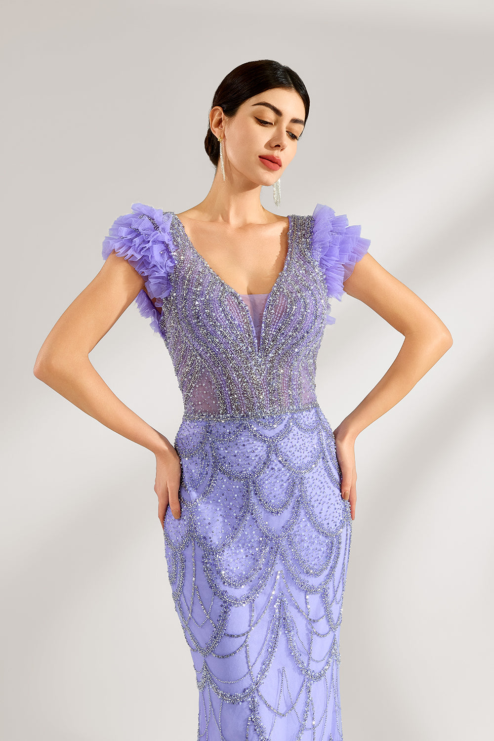 In soft lighting, a woman shines in a purple mermaid evening gown. It has sequin detailing, a V - neckline, and fluffy short sleeves, creating an elegant and glamorous look for formal events.5