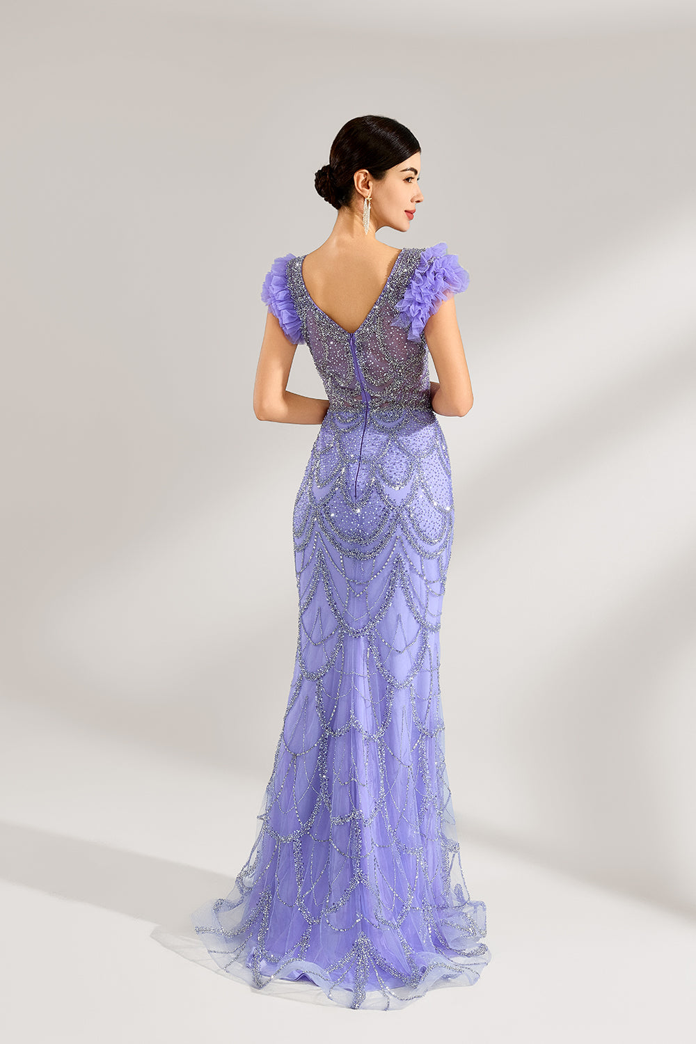 In soft lighting, a woman shines in a purple mermaid evening gown. It has sequin detailing, a V - neckline, and fluffy short sleeves, creating an elegant and glamorous look for formal events.2