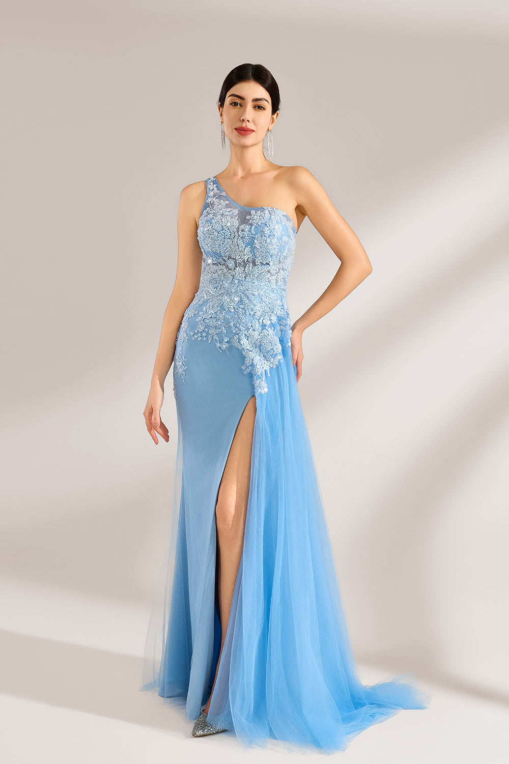 A woman with sleek dark hair and a poised stance wears a light - blue tulle gown. It has a one - shoulder design, lace - detailed bodice, and a high side slit. Paired with silver heels, the outfit radiates elegance, perfect for formal events like galas, blending romance and glamour.3