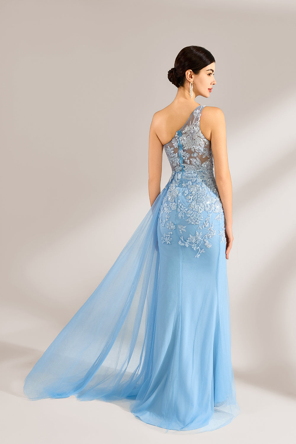 A woman with sleek dark hair and a poised stance wears a light - blue tulle gown. It has a one - shoulder design, lace - detailed bodice, and a high side slit. Paired with silver heels, the outfit radiates elegance, perfect for formal events like galas, blending romance and glamour.2