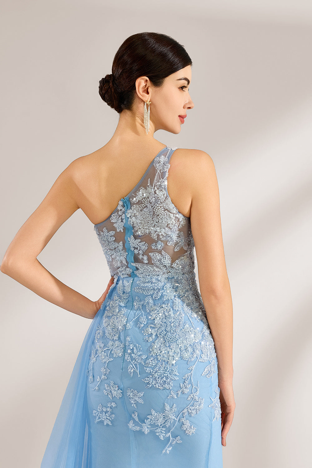 A woman with sleek dark hair and a poised stance wears a light - blue tulle gown. It has a one - shoulder design, lace - detailed bodice, and a high side slit. Paired with silver heels, the outfit radiates elegance, perfect for formal events like galas, blending romance and glamour.5