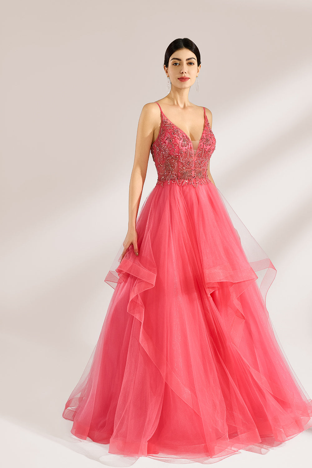 A woman stands against a light background, wearing a coral - pink tulle gown. It features thin straps, a deep V - neckline, and intricate bead embroidery on the bodice. The layered, ruffled tulle skirt creates a romantic and voluminous look, perfect for formal events like proms or weddings.4