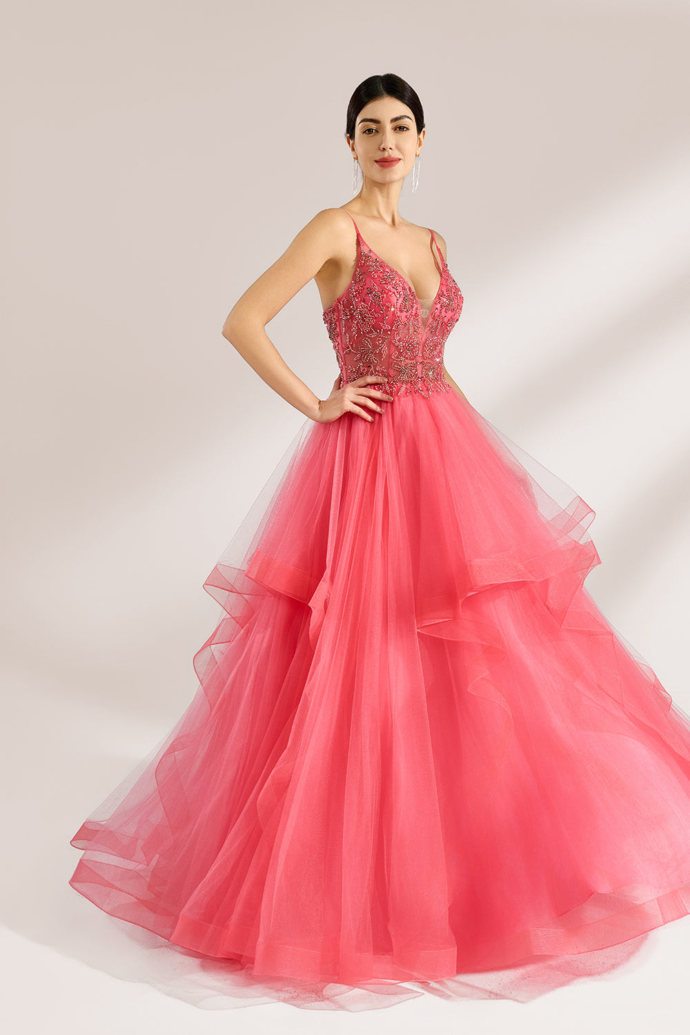 A woman stands against a light background, wearing a coral - pink tulle gown. It features thin straps, a deep V - neckline, and intricate bead embroidery on the bodice. The layered, ruffled tulle skirt creates a romantic and voluminous look, perfect for formal events like proms or weddings.3