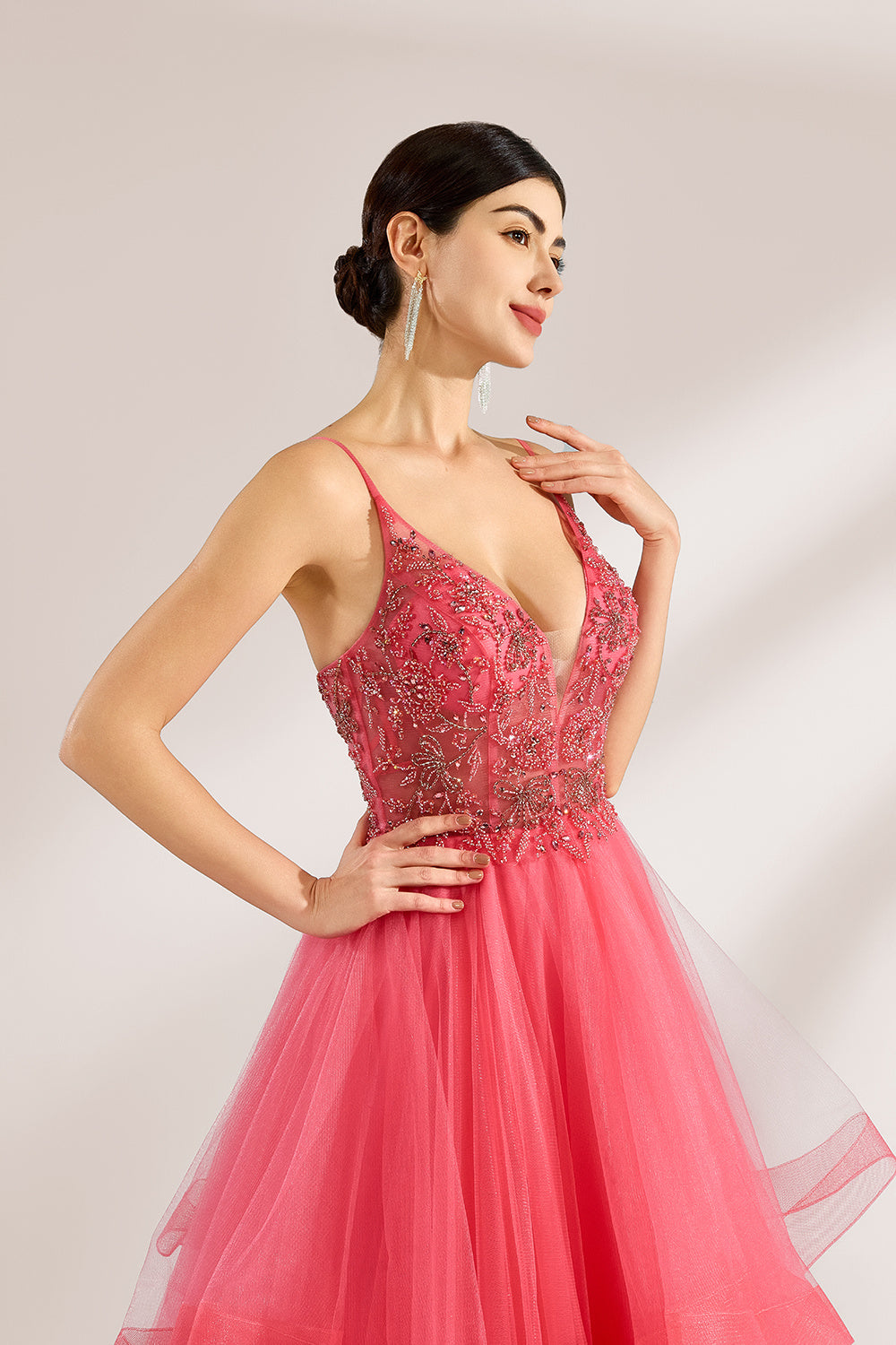 A woman stands against a light background, wearing a coral - pink tulle gown. It features thin straps, a deep V - neckline, and intricate bead embroidery on the bodice. The layered, ruffled tulle skirt creates a romantic and voluminous look, perfect for formal events like proms or weddings.5