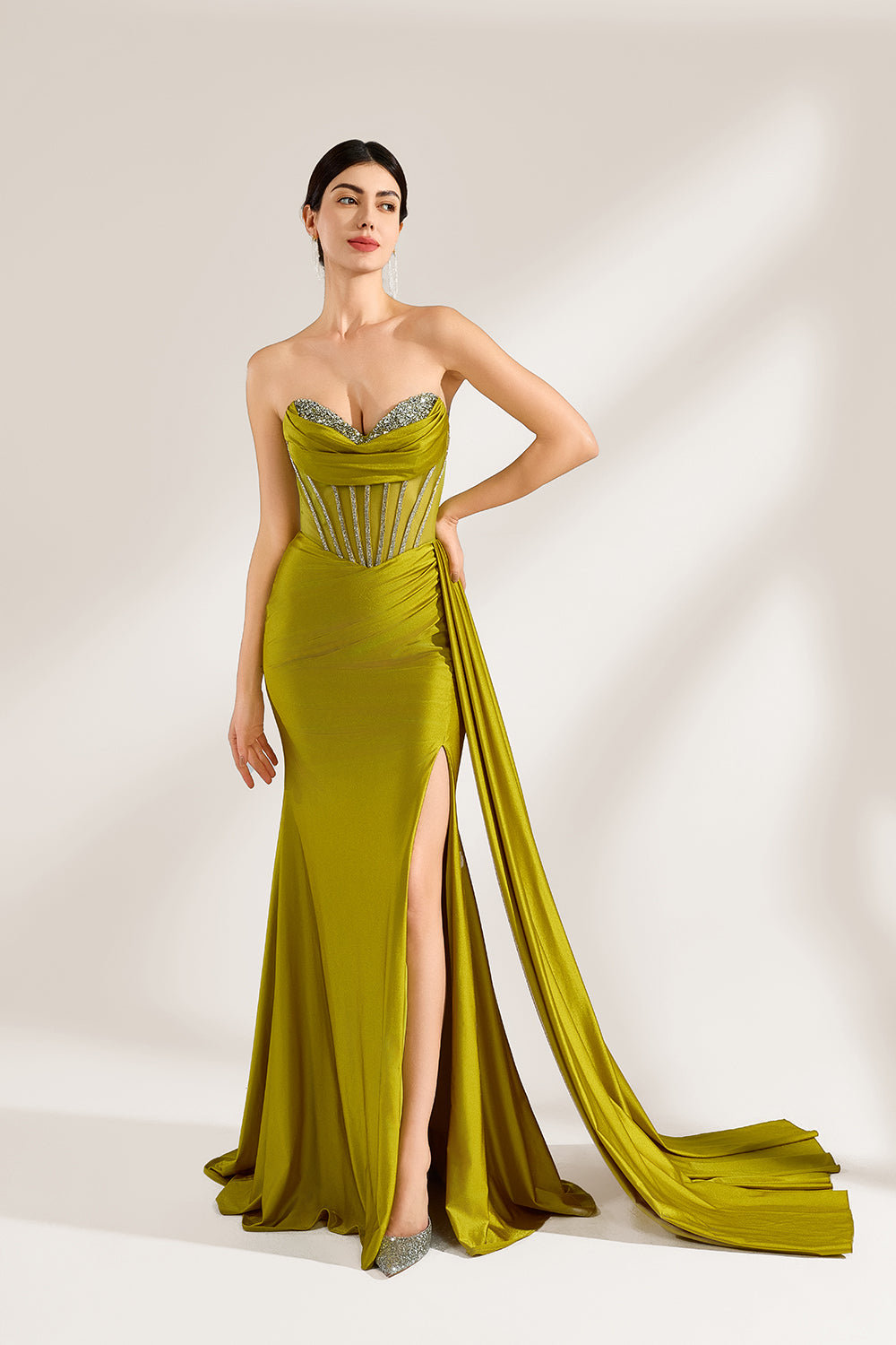 A woman stands against a light background, wearing an olive - green satin gown. It features a strapless neckline with crystal embellishments, a figure - hugging silhouette, a high side slit, and a dramatic train. The elegant details create a glamorous look, perfect for formal events like galas or red - carpet occasions.1