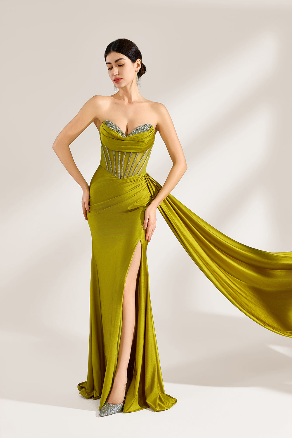 A woman stands against a light background, wearing an olive - green satin gown. It features a strapless neckline with crystal embellishments, a figure - hugging silhouette, a high side slit, and a dramatic train. The elegant details create a glamorous look, perfect for formal events like galas or red - carpet occasions.3