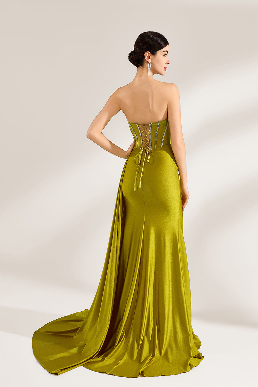 A woman stands against a light background, wearing an olive - green satin gown. It features a strapless neckline with crystal embellishments, a figure - hugging silhouette, a high side slit, and a dramatic train. The elegant details create a glamorous look, perfect for formal events like galas or red - carpet occasions.2