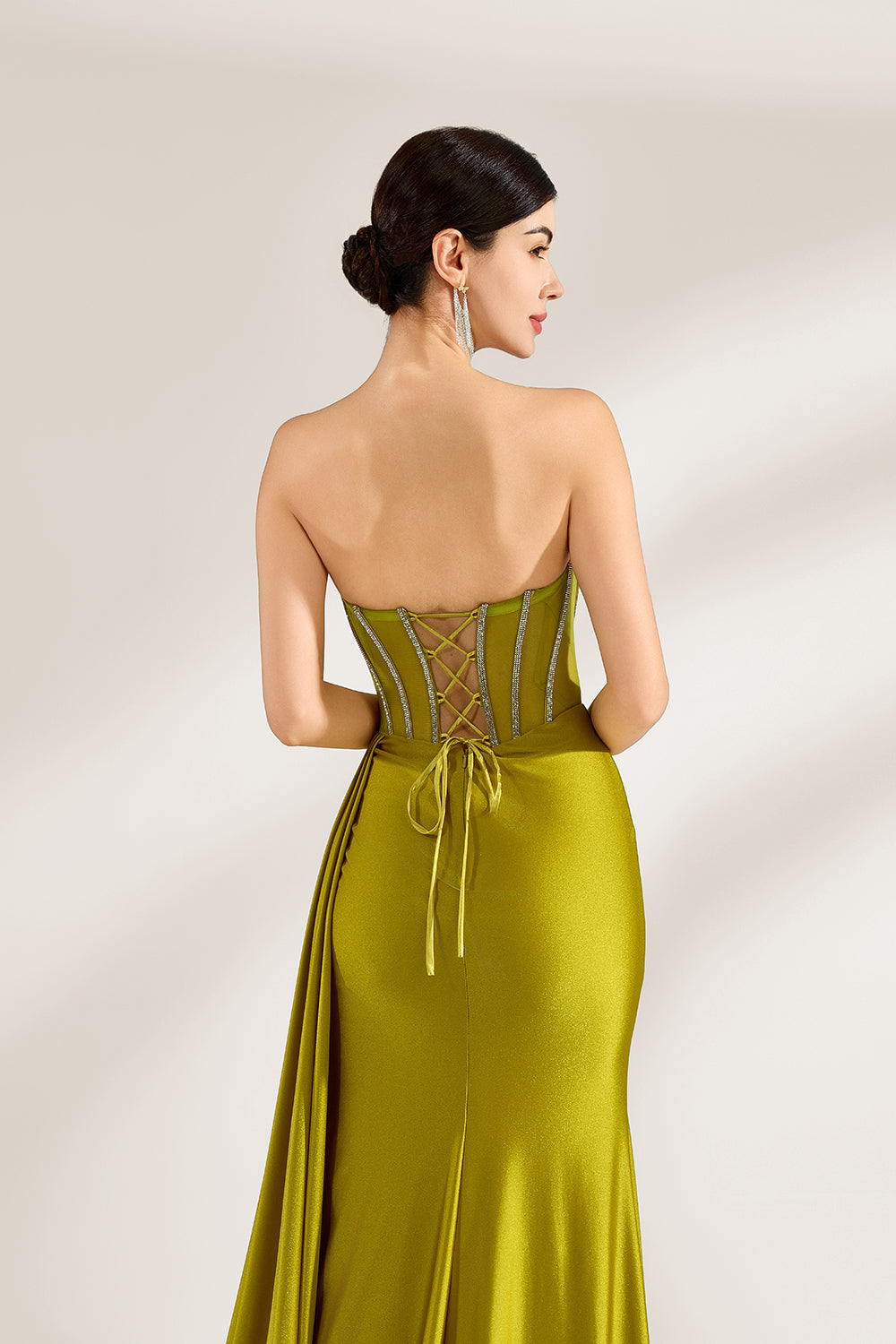 A woman stands against a light background, wearing an olive - green satin gown. It features a strapless neckline with crystal embellishments, a figure - hugging silhouette, a high side slit, and a dramatic train. The elegant details create a glamorous look, perfect for formal events like galas or red - carpet occasions.6