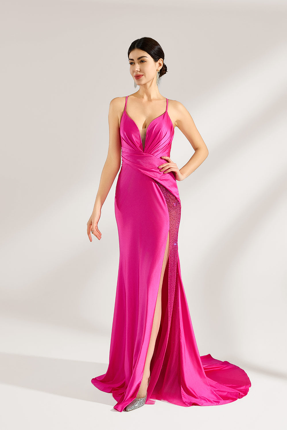 A woman stands against a light background, wearing a hot - pink satin gown. It features thin straps, a deep V - neckline, a draped bodice, a high side slit with crystal embellishments, and a trailing skirt. The elegant design creates a glamorous look, perfect for formal events like galas or red - carpet occasions.1