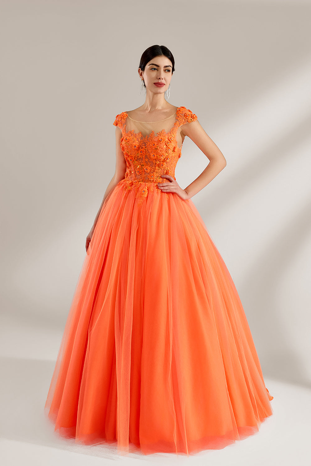 Presented against a light backdrop, a woman dons an orange ball - gown style dress. It features a sheer neckline with delicate floral lace embroidery on the bodice, and a voluminous tulle skirt. The vibrant design creates a lively and elegant look, perfect for formal events like proms or weddings.1
