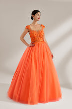 Presented against a light backdrop, a woman dons an orange ball - gown style dress. It features a sheer neckline with delicate floral lace embroidery on the bodice, and a voluminous tulle skirt. The vibrant design creates a lively and elegant look, perfect for formal events like proms or weddings.3