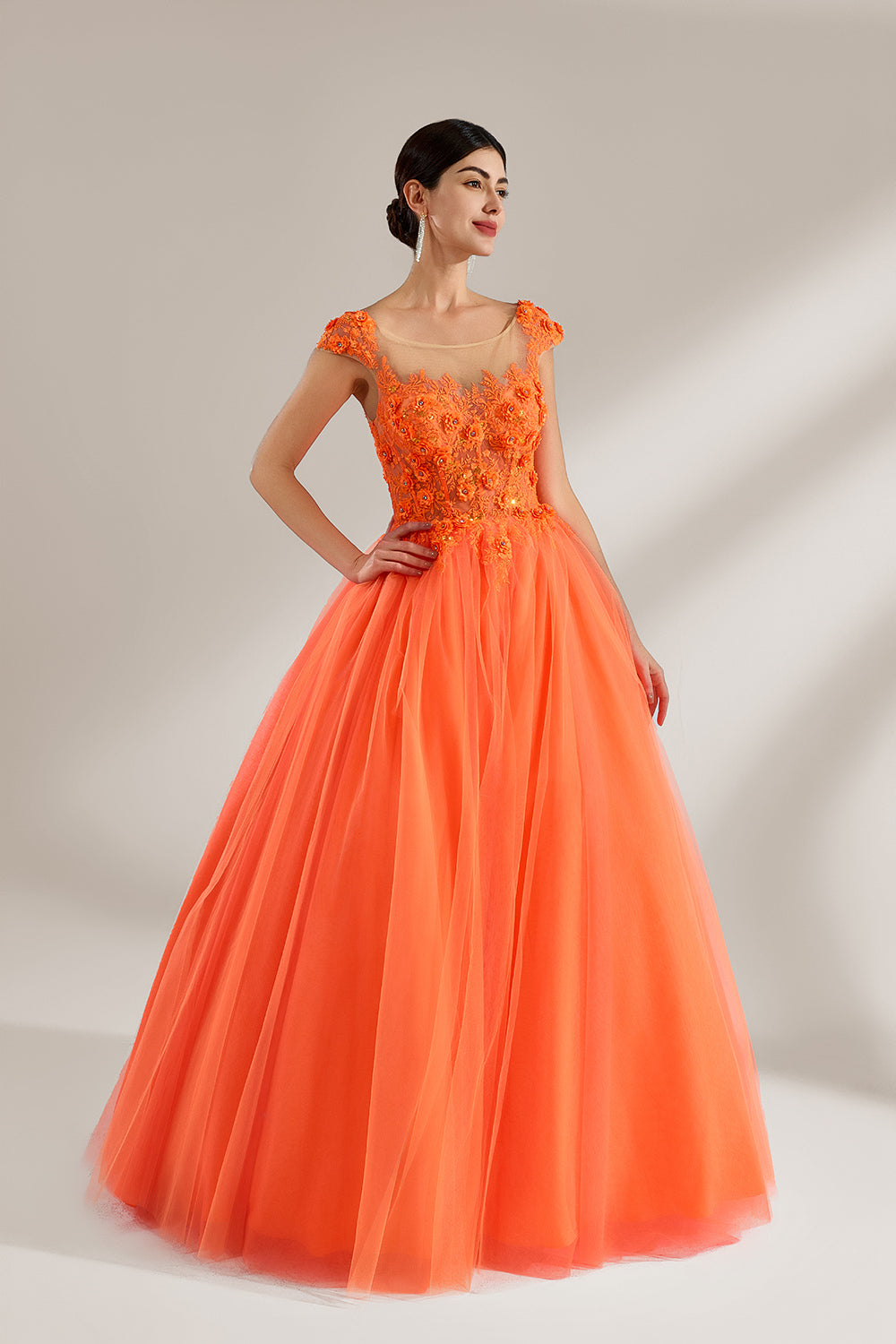 Presented against a light backdrop, a woman dons an orange ball - gown style dress. It features a sheer neckline with delicate floral lace embroidery on the bodice, and a voluminous tulle skirt. The vibrant design creates a lively and elegant look, perfect for formal events like proms or weddings.3