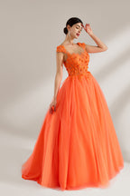Presented against a light backdrop, a woman dons an orange ball - gown style dress. It features a sheer neckline with delicate floral lace embroidery on the bodice, and a voluminous tulle skirt. The vibrant design creates a lively and elegant look, perfect for formal events like proms or weddings.