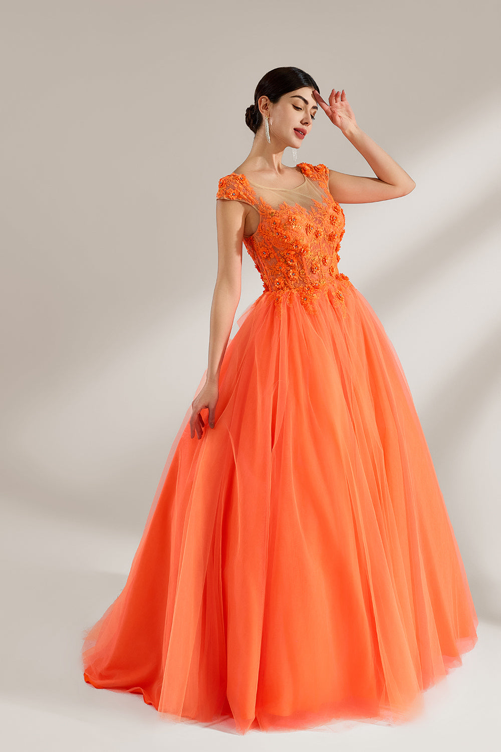 Presented against a light backdrop, a woman dons an orange ball - gown style dress. It features a sheer neckline with delicate floral lace embroidery on the bodice, and a voluminous tulle skirt. The vibrant design creates a lively and elegant look, perfect for formal events like proms or weddings.