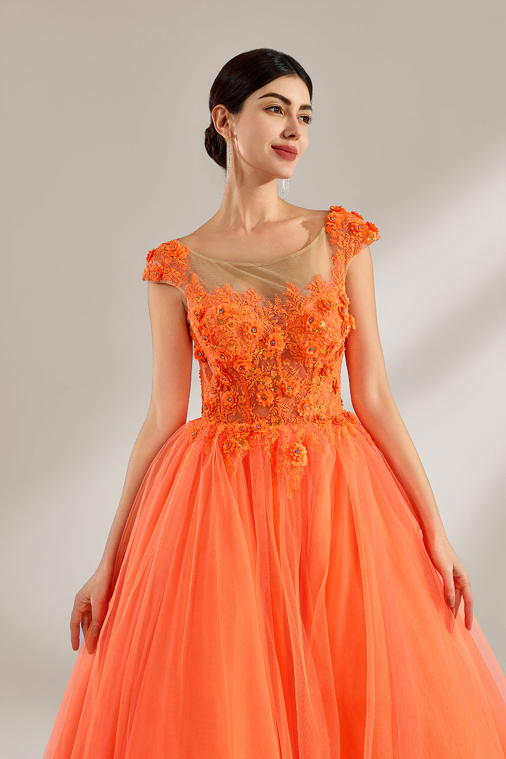 Presented against a light backdrop, a woman dons an orange ball - gown style dress. It features a sheer neckline with delicate floral lace embroidery on the bodice, and a voluminous tulle skirt. The vibrant design creates a lively and elegant look, perfect for formal events like proms or weddings.4