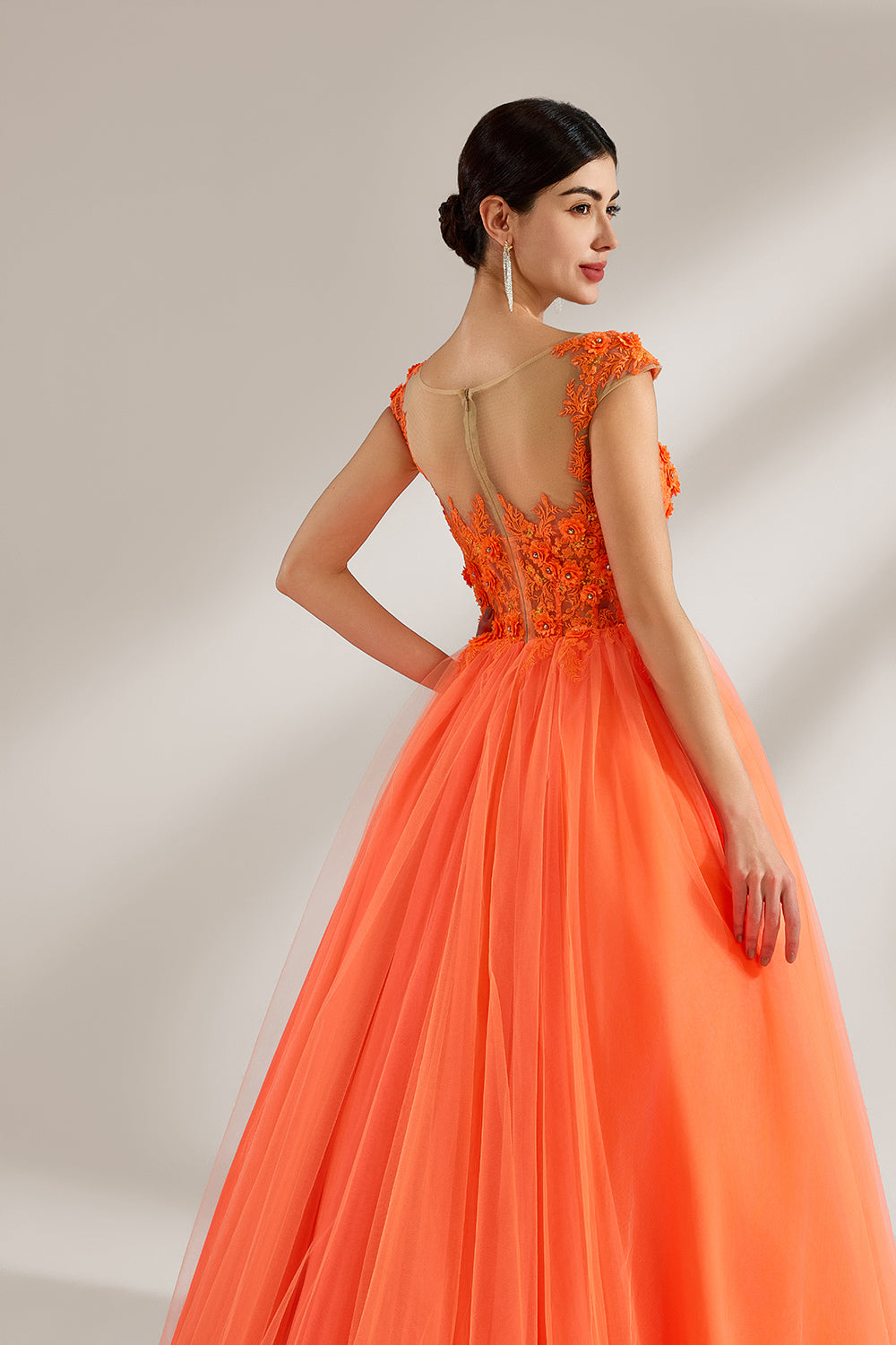Presented against a light backdrop, a woman dons an orange ball - gown style dress. It features a sheer neckline with delicate floral lace embroidery on the bodice, and a voluminous tulle skirt. The vibrant design creates a lively and elegant look, perfect for formal events like proms or weddings.5