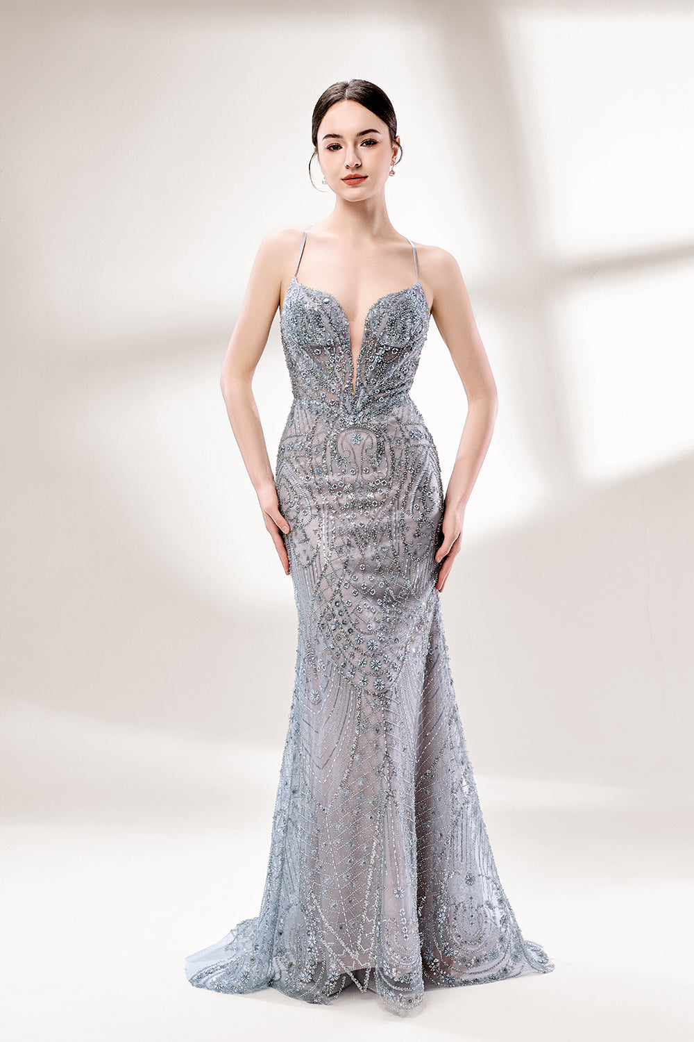 A woman stands against a light - hued background, wearing a light - grey, sheer gown adorned with intricate silver - toned bead patterns. It has thin straps, a deep V - neckline, and a mermaid silhouette. The detailed beadwork and sheer fabric create a glamorous look, perfect for proms or formal parties, radiating sophistication.1