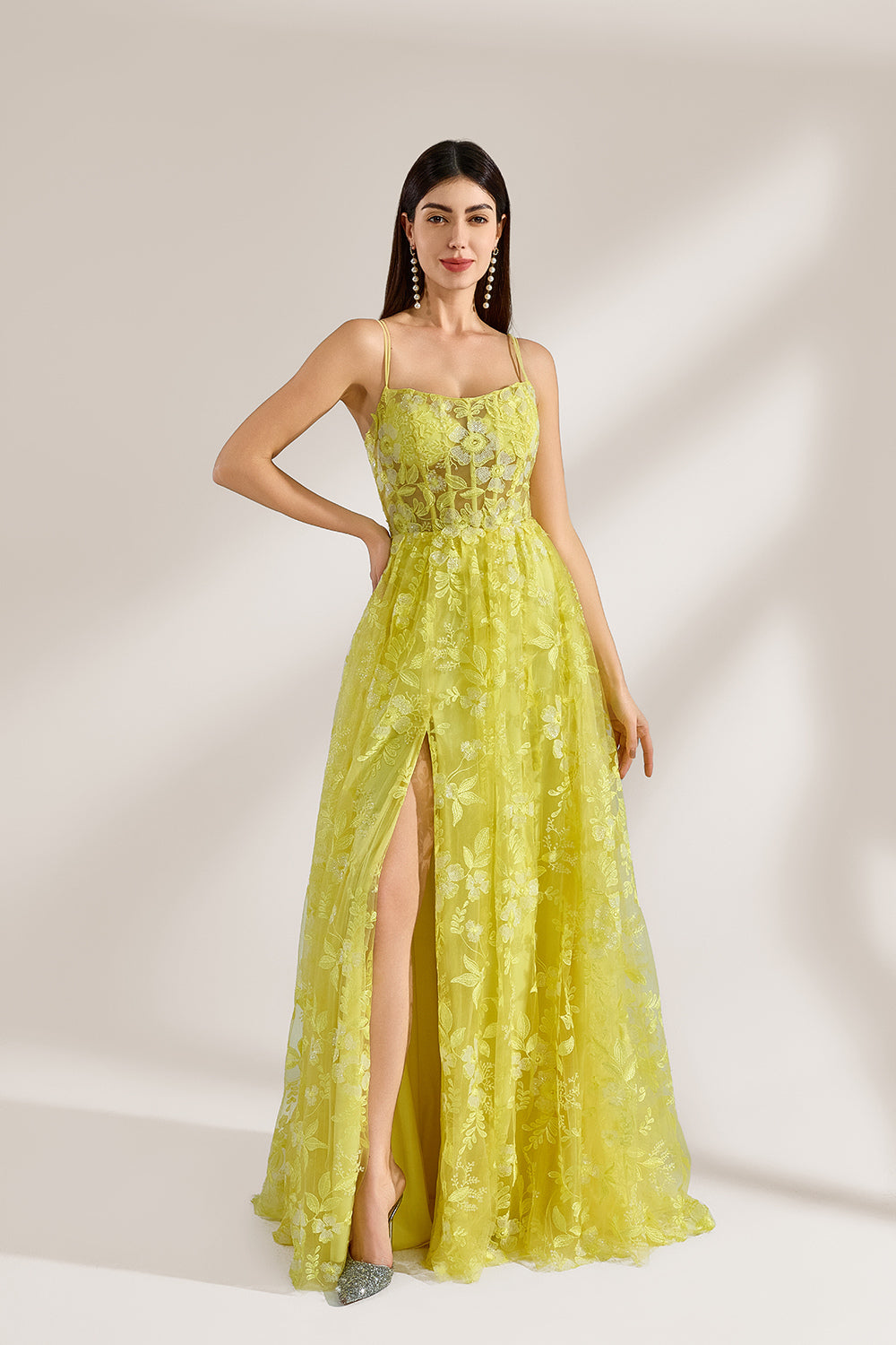 Bathed in soft light, a woman dazzles in a yellow floral - patterned gown. It has thin straps, a fitted bodice, and a high side slit. The flowing skirt creates an elegant and vibrant look, perfect for formal events or special occasions.3