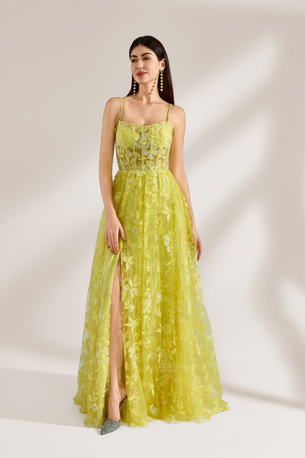 Bathed in soft light, a woman dazzles in a yellow floral - patterned gown. It has thin straps, a fitted bodice, and a high side slit. The flowing skirt creates an elegant and vibrant look, perfect for formal events or special occasions.4