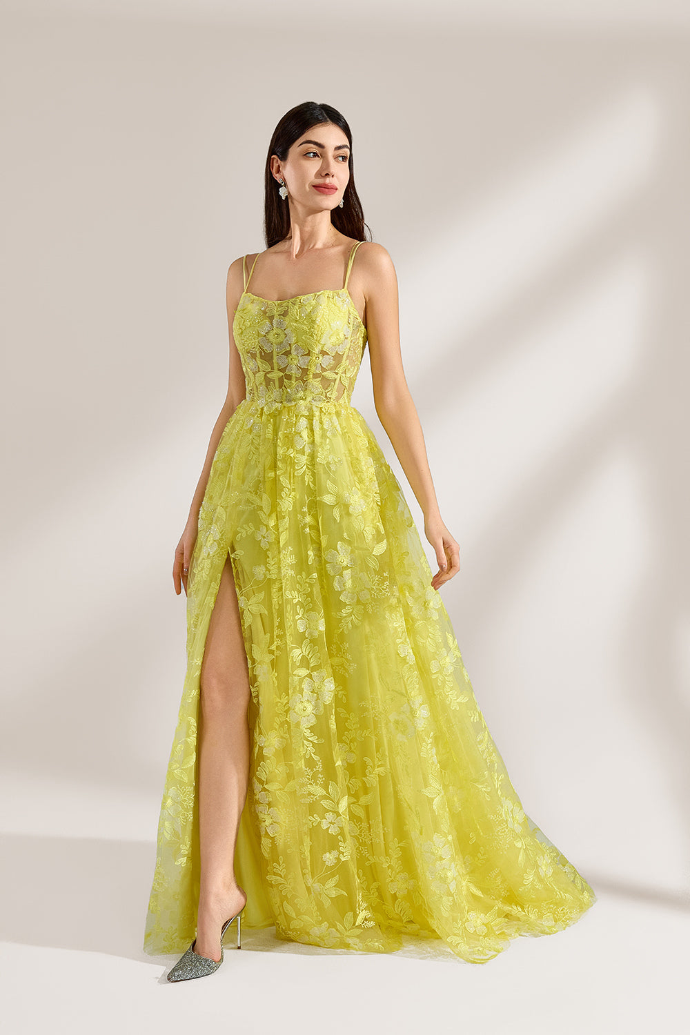 Bathed in soft light, a woman dazzles in a yellow floral - patterned gown. It has thin straps, a fitted bodice, and a high side slit. The flowing skirt creates an elegant and vibrant look, perfect for formal events or special occasions.1