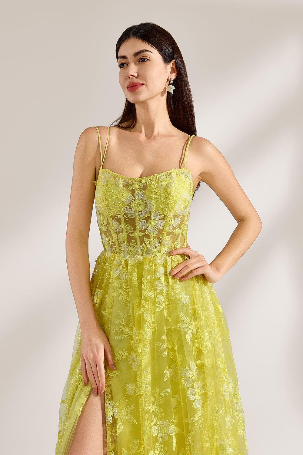 Bathed in soft light, a woman dazzles in a yellow floral - patterned gown. It has thin straps, a fitted bodice, and a high side slit. The flowing skirt creates an elegant and vibrant look, perfect for formal events or special occasions.5