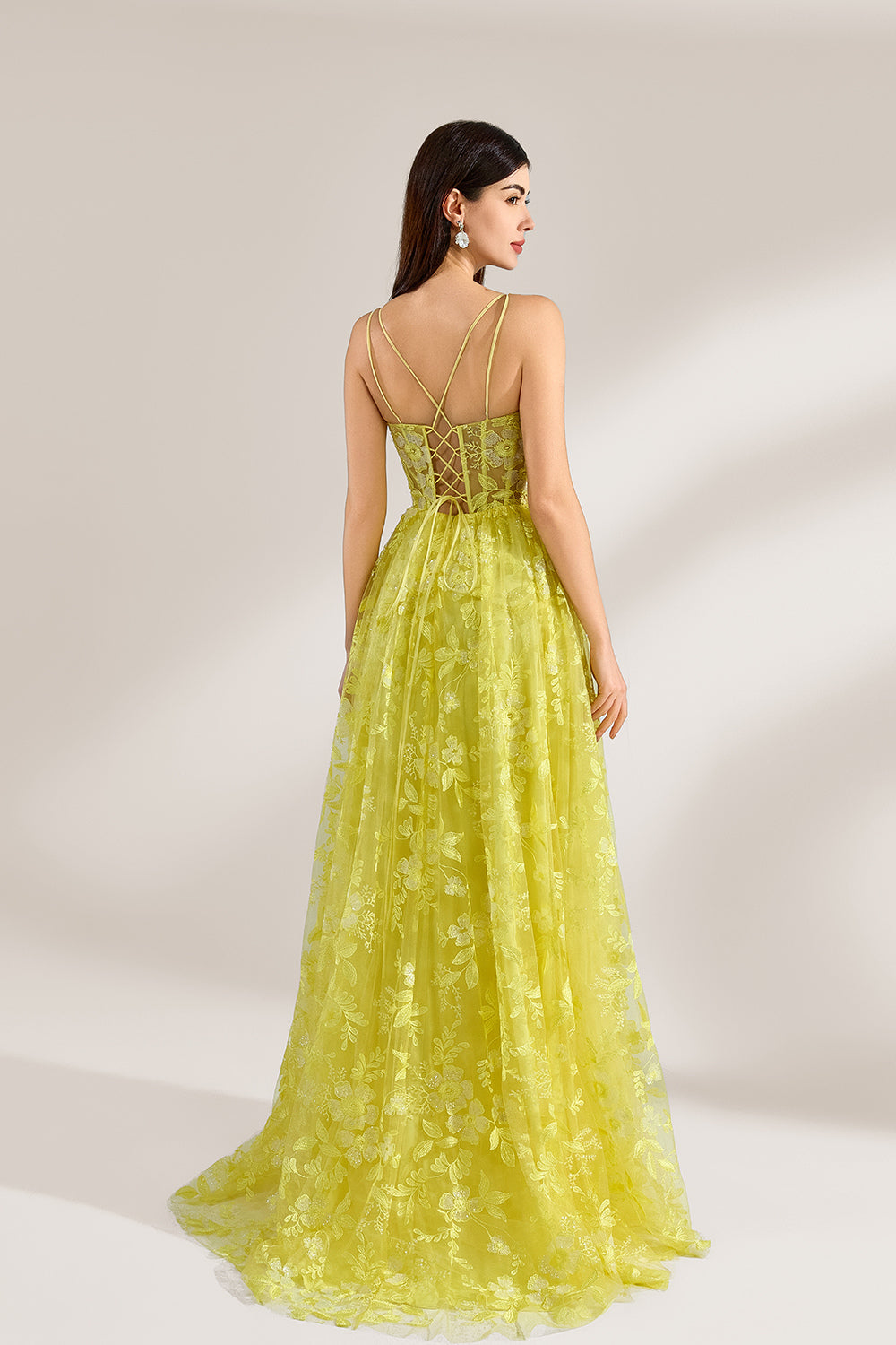 Bathed in soft light, a woman dazzles in a yellow floral - patterned gown. It has thin straps, a fitted bodice, and a high side slit. The flowing skirt creates an elegant and vibrant look, perfect for formal events or special occasions.2