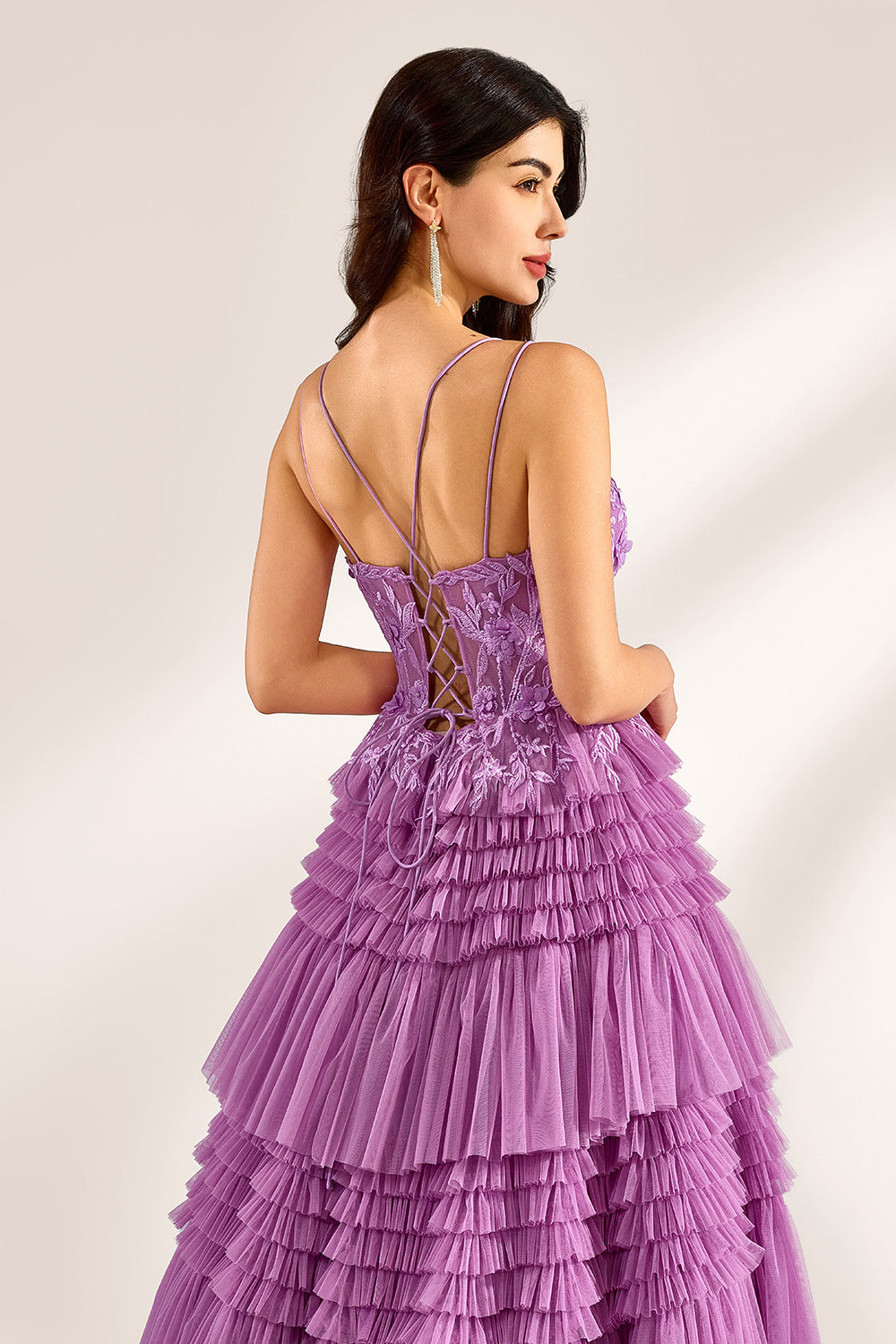 A woman stands against a light background, wearing a lavender tulle gown. It has thin straps, a deep V - neckline, and intricate floral lace embroidery on the bodice. The multi - layered, ruffled tulle skirt with a train creates a romantic and voluminous look, perfect for formal events like weddings or proms, exuding elegance and charm.6