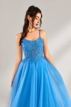 A woman stands against a light background, wearing a blue tulle gown. It features thin straps, a square neckline, intricate lace embroidery on the bodice, and a voluminous tulle skirt with subtle glitter. The elegant design creates a romantic and glamorous look, perfect for formal events like proms or weddings.5