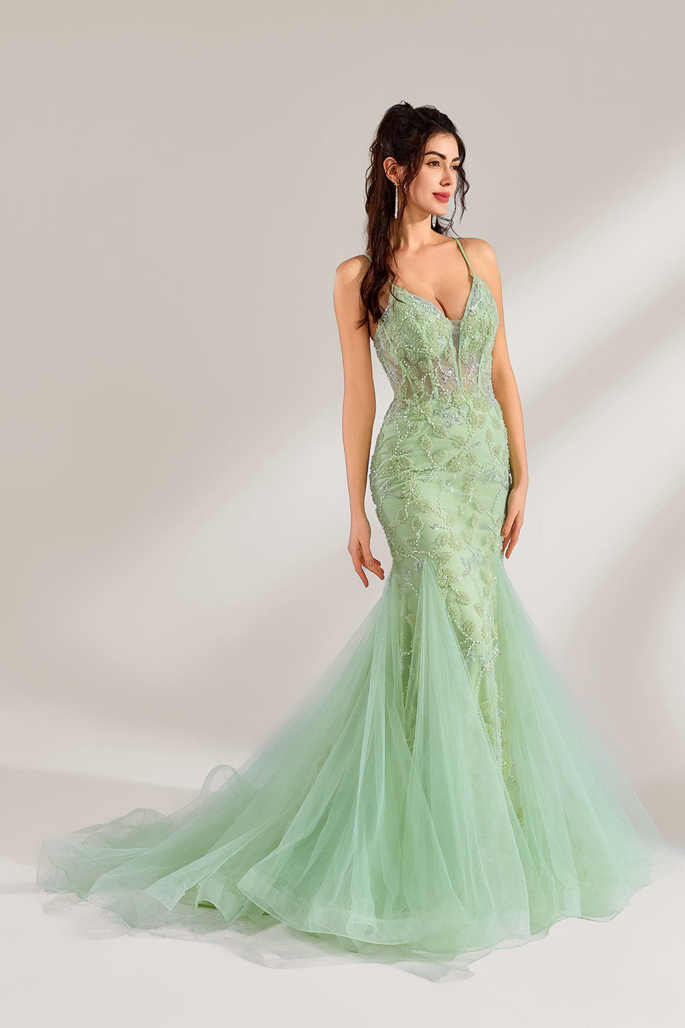 The model wearing it has long, wavy hair tied up in a half-up style, and she accessorizes with elegant earrings. The dress adopts a fresh light green color. The spaghetti strap design reveals the graceful shoulder and neck lines, and the deep V-neck adds a touch of sexiness. The mermaid skirt is paired with light tulle, embellished with exquisite embroidery and beading, making the whole dress look elegant and luxurious. It is very suitable for formal occasions such as dinners and weddings.1