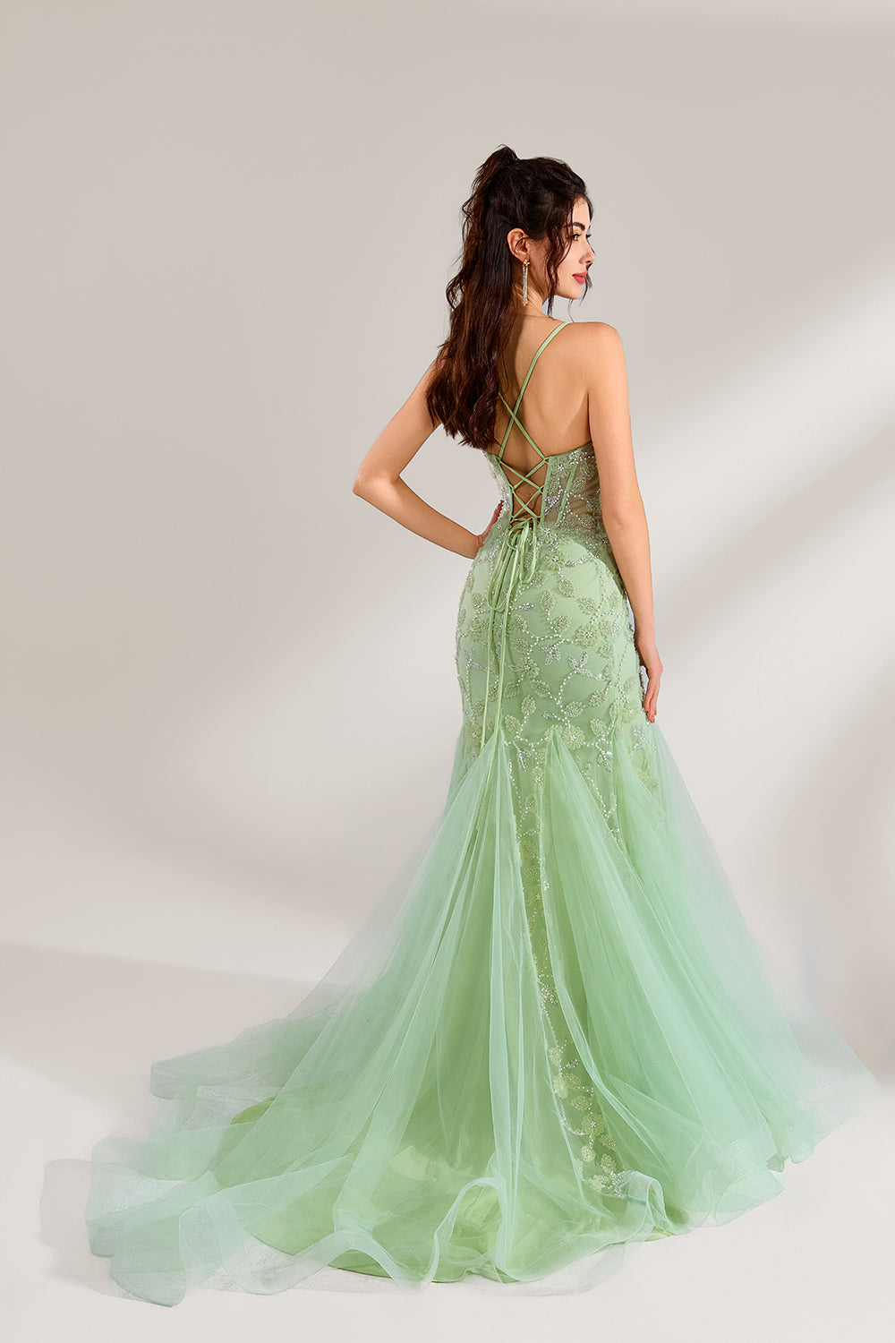The model wearing it has long, wavy hair tied up in a half-up style, and she accessorizes with elegant earrings. The dress adopts a fresh light green color. The spaghetti strap design reveals the graceful shoulder and neck lines, and the deep V-neck adds a touch of sexiness. The mermaid skirt is paired with light tulle, embellished with exquisite embroidery and beading, making the whole dress look elegant and luxurious. It is very suitable for formal occasions such as dinners and weddings.2