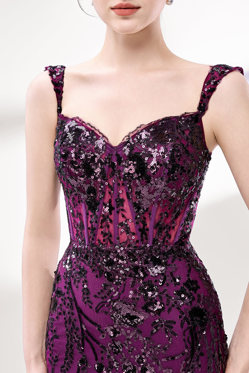 Set against a light background, a woman wears a purple tulle gown embellished with sequin embroidery. It has thin straps, a sweetheart neckline, a sheer bodice patterned with florals, and a mermaid skirt with a high side slit. Silver heels complete the look, with the sparkling sequins and refined silhouette ideal for proms or formal dinners.3