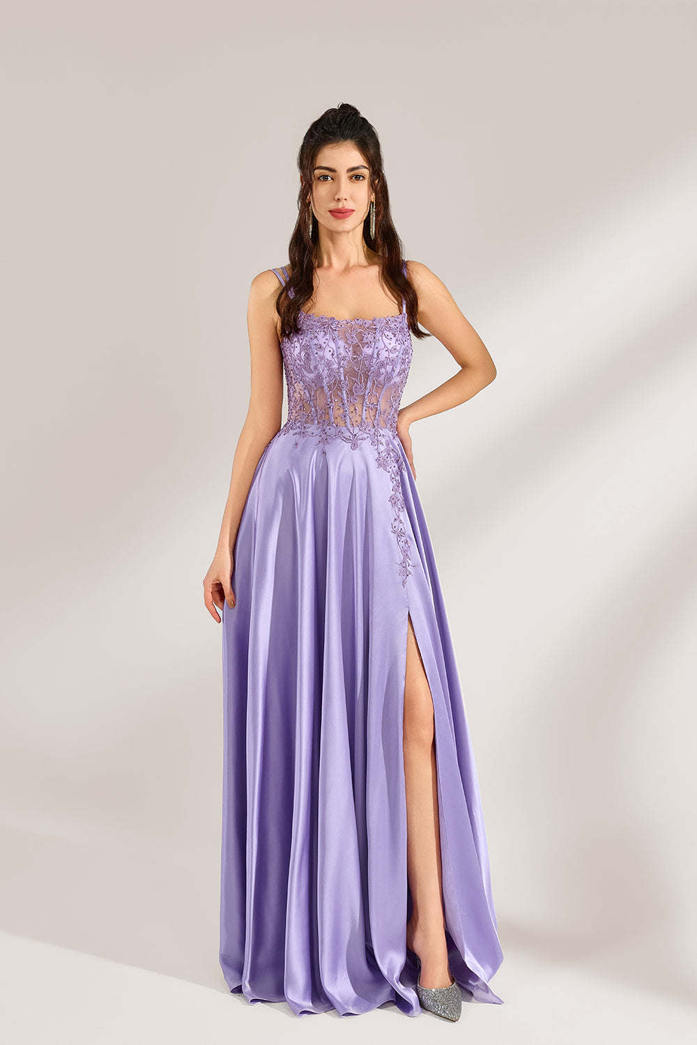 A woman with long, wavy dark hair and a confident pose wears a light - purple satin gown. It has thin straps, a sheer lace - detailed bodice, and a high side slit. Paired with silver - tone heels, the outfit radiates elegance, perfect for formal events like galas or evening receptions.4