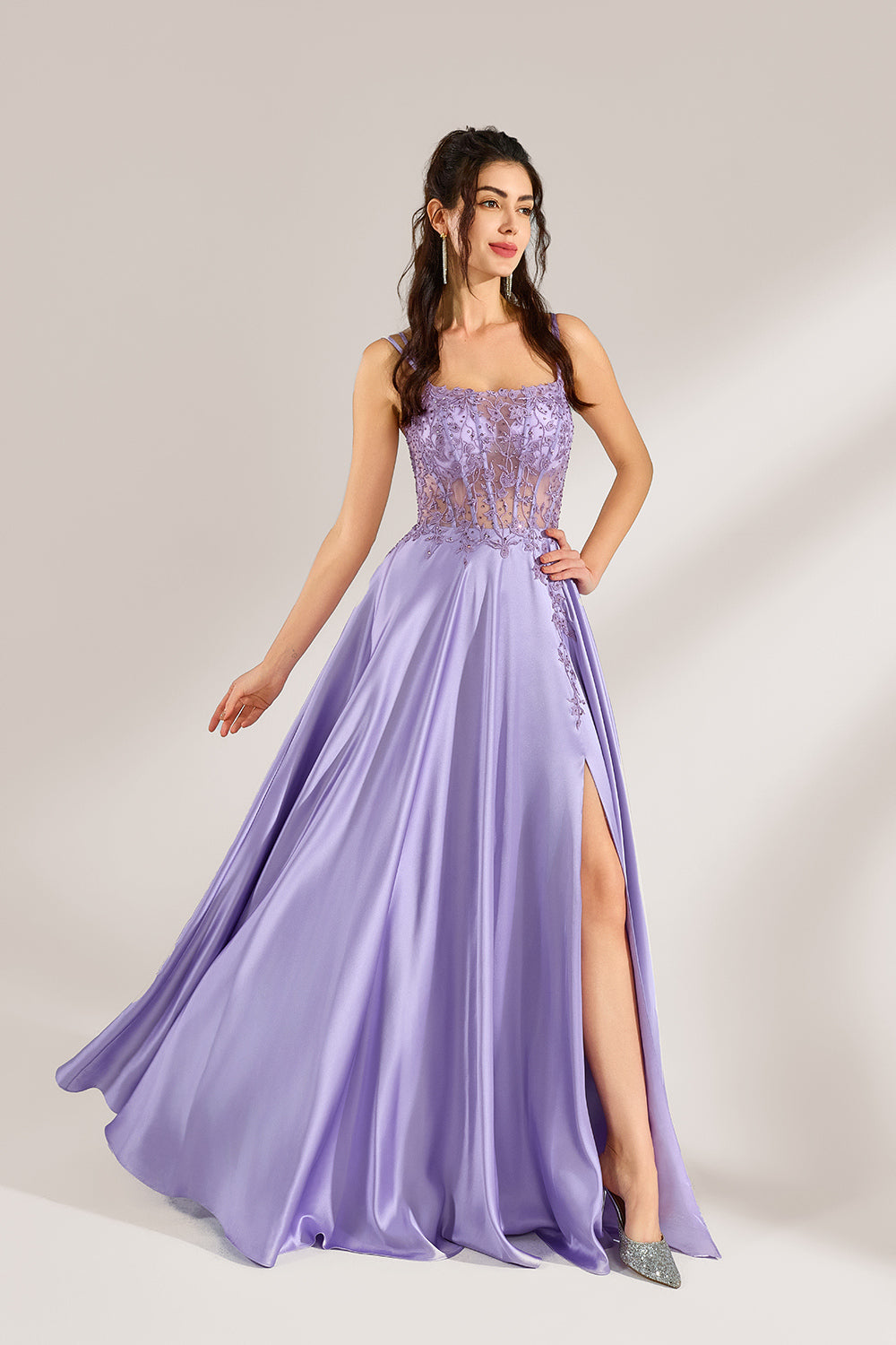 A woman with long, wavy dark hair and a confident pose wears a light - purple satin gown. It has thin straps, a sheer lace - detailed bodice, and a high side slit. Paired with silver - tone heels, the outfit radiates elegance, perfect for formal events like galas or evening receptions.3