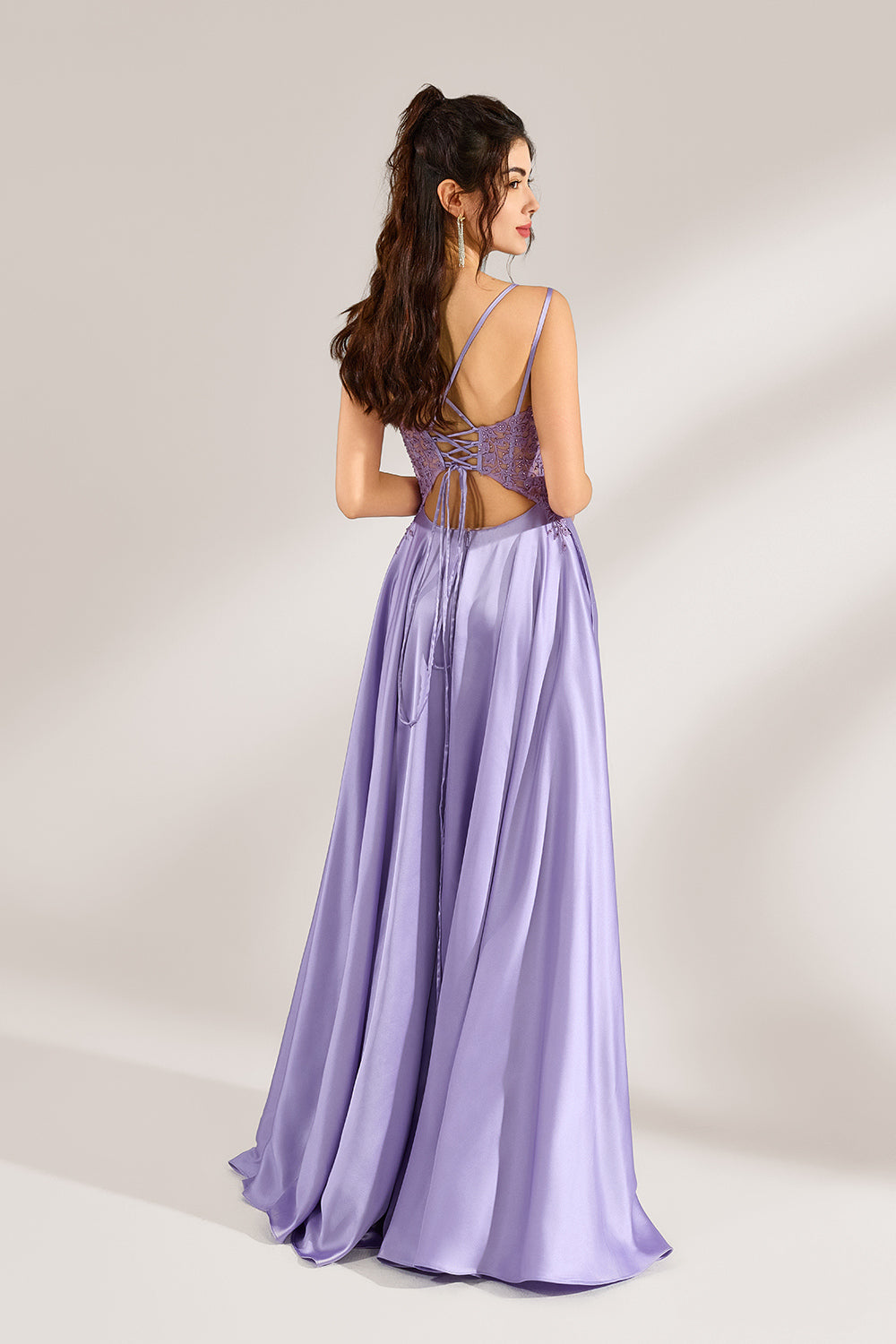 A woman with long, wavy dark hair and a confident pose wears a light - purple satin gown. It has thin straps, a sheer lace - detailed bodice, and a high side slit. Paired with silver - tone heels, the outfit radiates elegance, perfect for formal events like galas or evening receptions.2