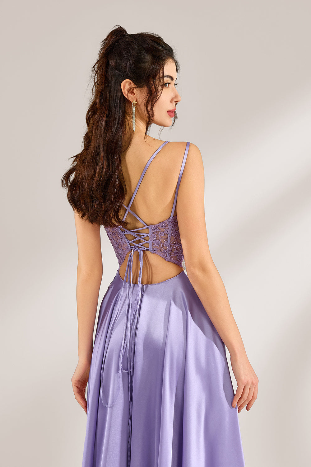 A woman with long, wavy dark hair and a confident pose wears a light - purple satin gown. It has thin straps, a sheer lace - detailed bodice, and a high side slit. Paired with silver - tone heels, the outfit radiates elegance, perfect for formal events like galas or evening receptions.6