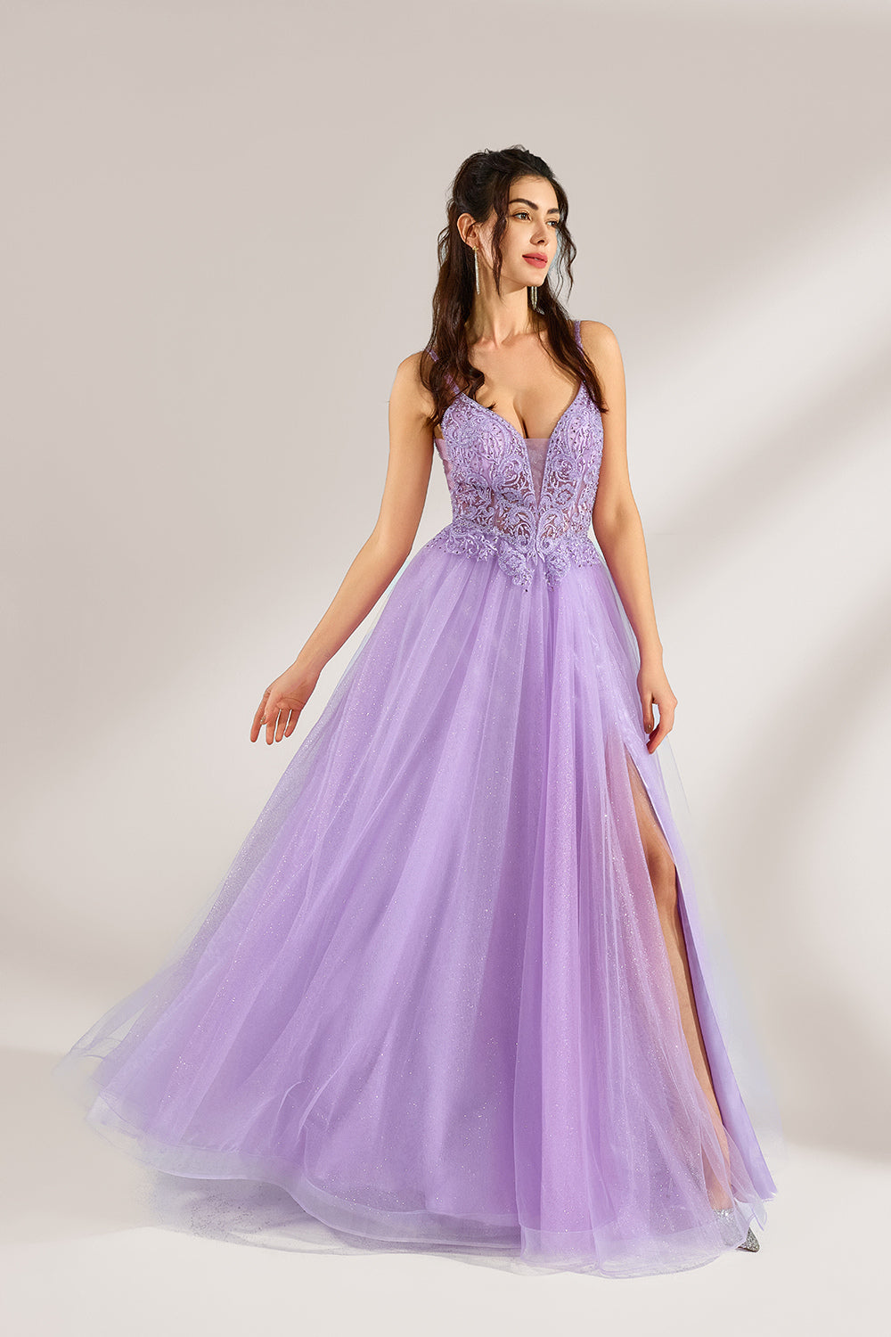 Against a light - hued background, a woman adorns a lavender tulle gown. It has thin straps, a deep V - neckline with delicate lace embroidery on the bodice, and a high side slit. The voluminous tulle skirt, shimmering faintly, gives off an elegant and romantic vibe, ideal for formal events such as proms or weddings.1
