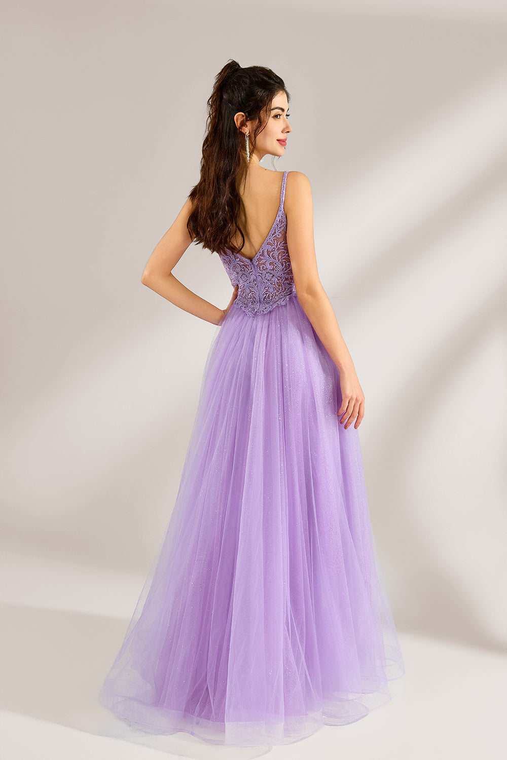 Against a light - hued background, a woman adorns a lavender tulle gown. It has thin straps, a deep V - neckline with delicate lace embroidery on the bodice, and a high side slit. The voluminous tulle skirt, shimmering faintly, gives off an elegant and romantic vibe, ideal for formal events such as proms or weddings.2