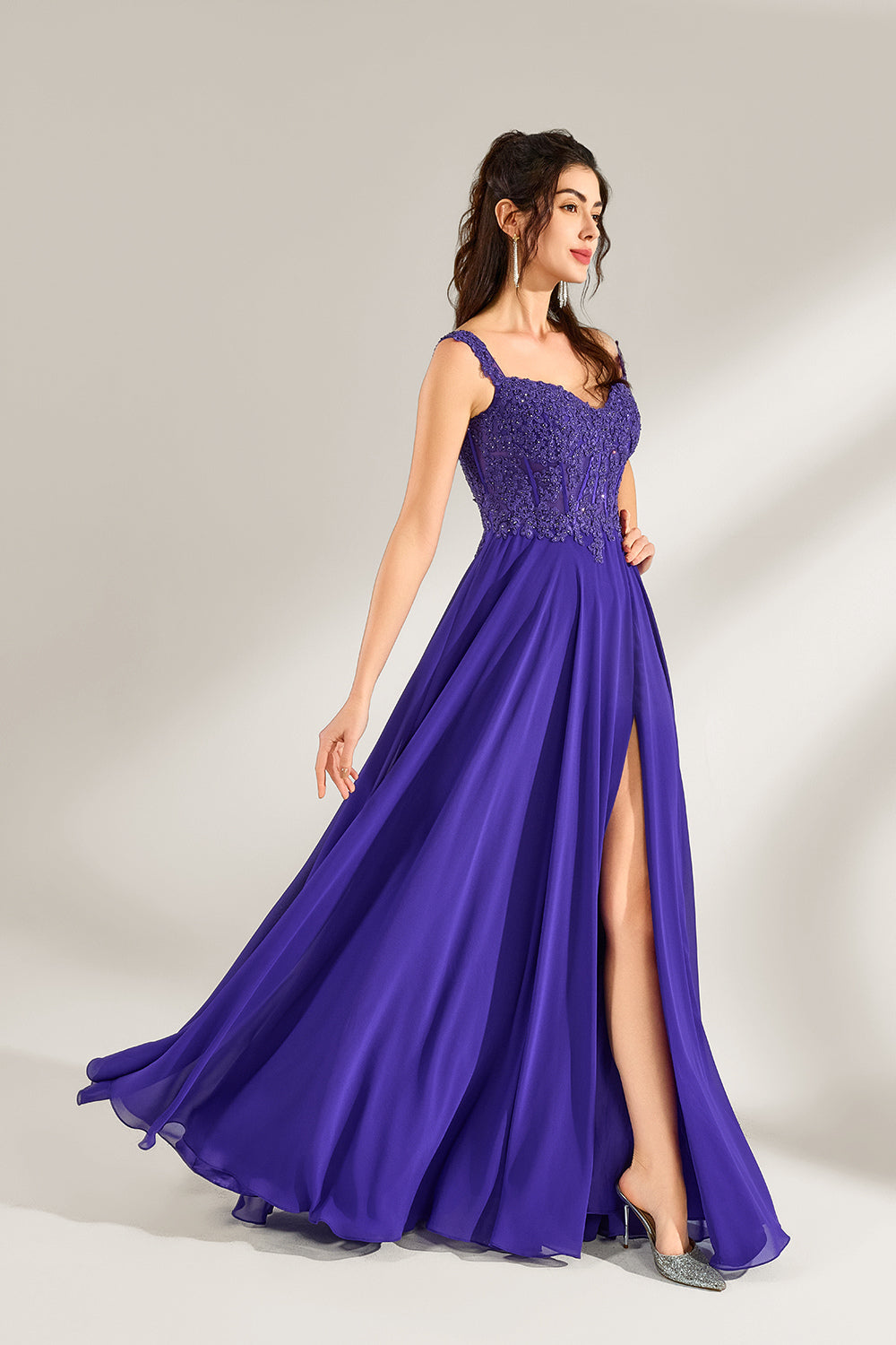 Against a light backdrop, a woman is seen in a purple chiffon gown. It comes with wide straps, a sweetheart neckline, and the bodice is decorated with intricate lace embroidery. There's also a high side slit, and the flowing chiffon skirt gives an elegant and graceful appearance, ideal for formal events such as proms or weddings.3