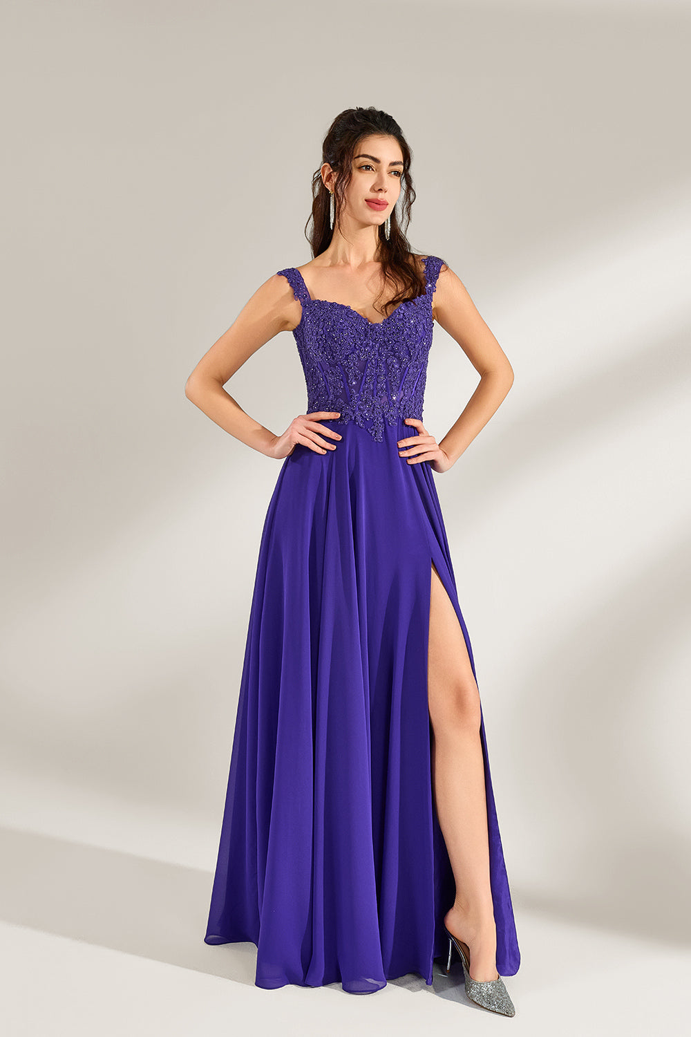 Against a light backdrop, a woman is seen in a purple chiffon gown. It comes with wide straps, a sweetheart neckline, and the bodice is decorated with intricate lace embroidery. There's also a high side slit, and the flowing chiffon skirt gives an elegant and graceful appearance, ideal for formal events such as proms or weddings.4