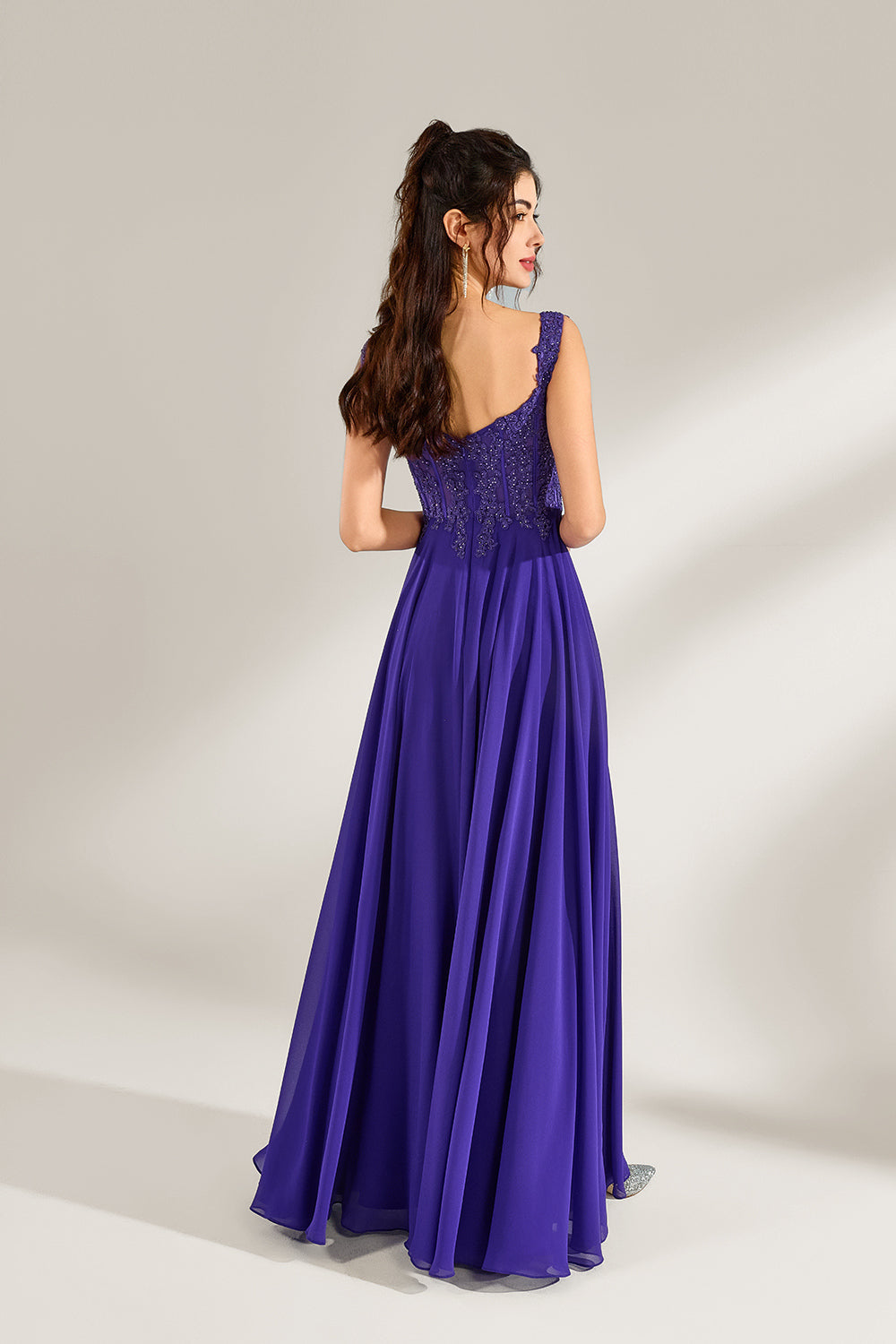 Against a light backdrop, a woman is seen in a purple chiffon gown. It comes with wide straps, a sweetheart neckline, and the bodice is decorated with intricate lace embroidery. There's also a high side slit, and the flowing chiffon skirt gives an elegant and graceful appearance, ideal for formal events such as proms or weddings.2