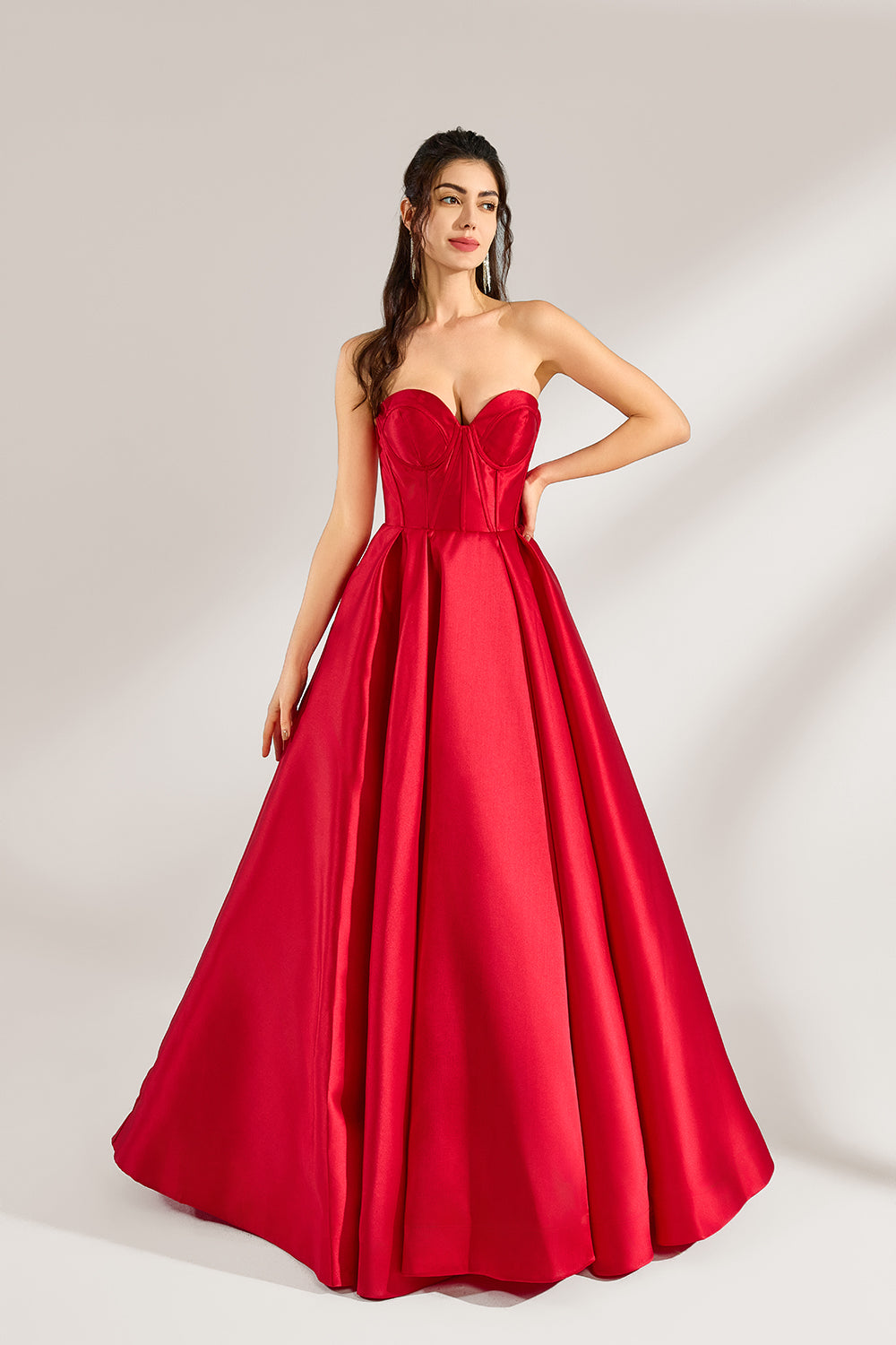 A woman stands against a light background, wearing a red satin strapless ball gown. The sweetheart neckline and voluminous skirt create an elegant and classic look, perfect for formal events like proms or weddings.1